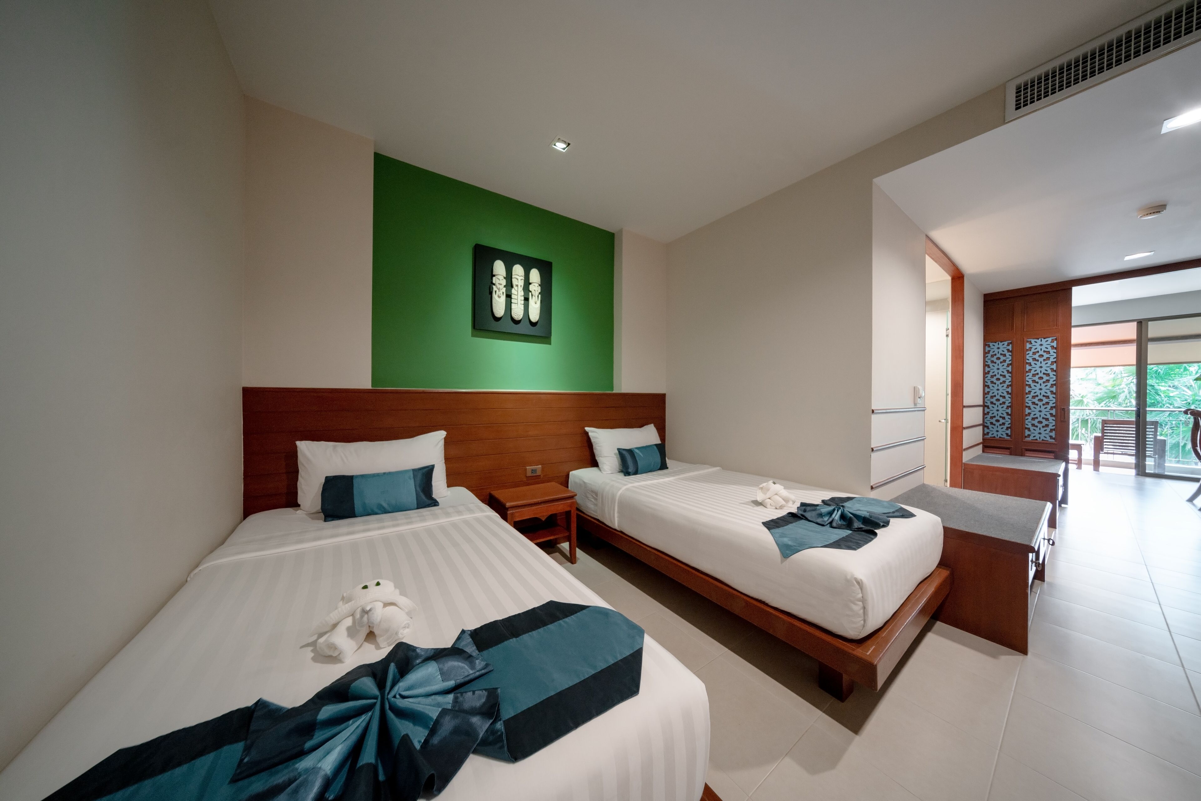 A hotel room with two beds, a green accent wall, and a view of the outdoors.