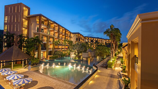 Un hotel con piscina, mobiliario exterior y una fachada iluminada.