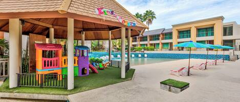 A children's play area with colorful structures and a pool in the background.