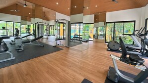 Un gimnasio espacioso con diversos equipos de ejercicio, ventanas amplias y techo de madera.