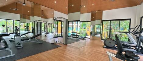 A spacious gym with various exercise equipment, large windows, and wooden ceiling.