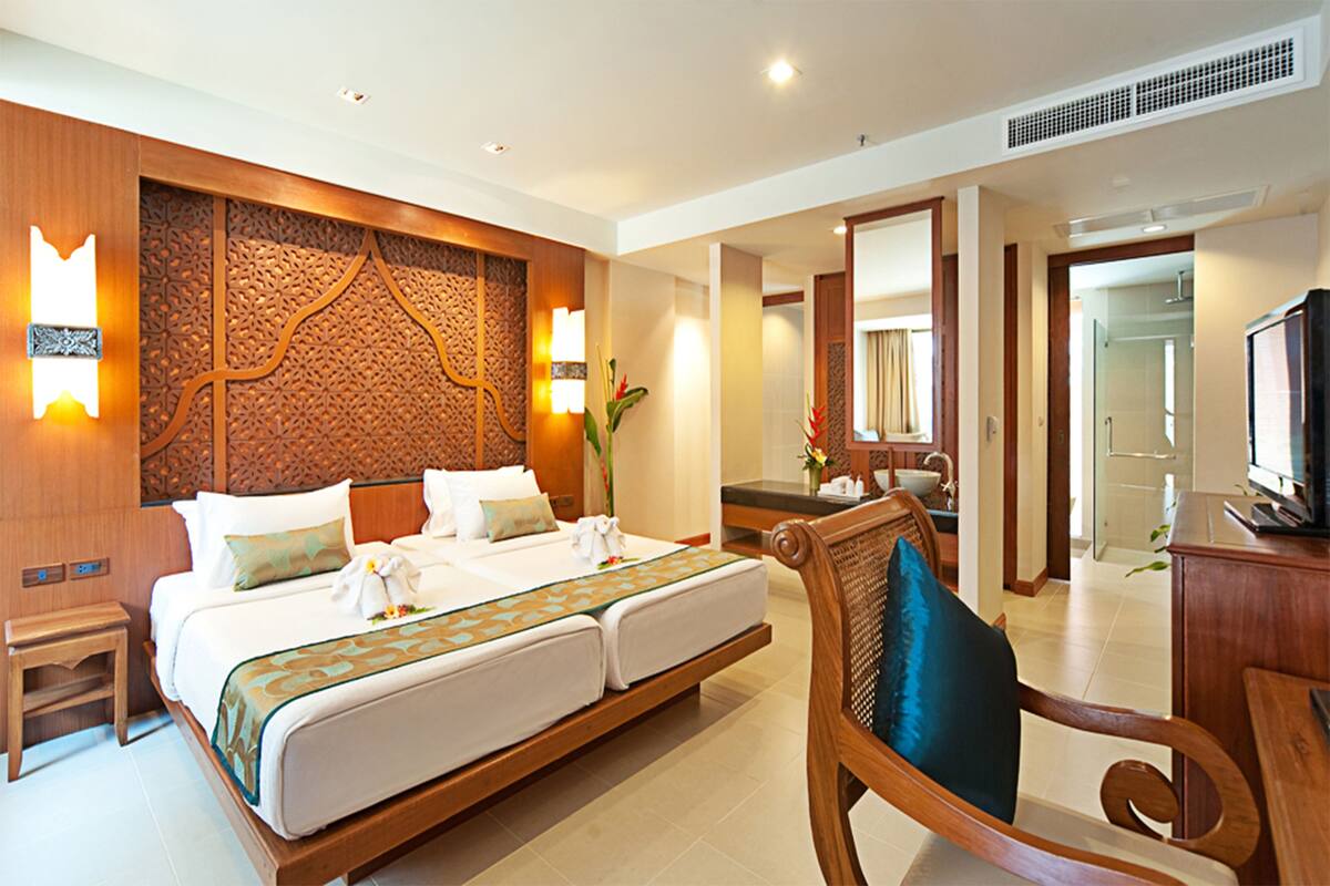 A hotel room with a large bed, a wooden headboard, a television, and a bathroom visible through an open door.