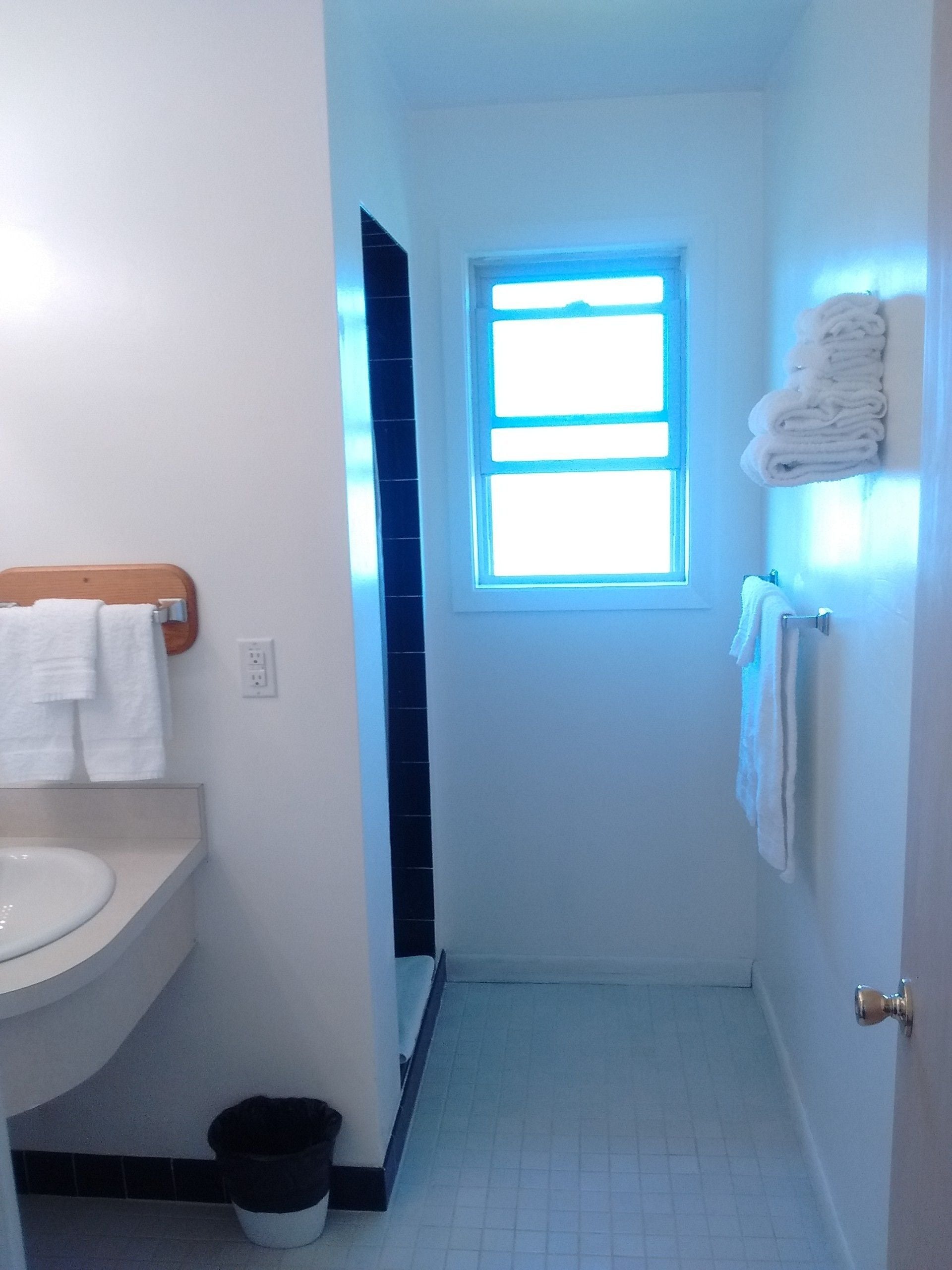 A narrow bathroom with a white sink, a window, and a towel rack.