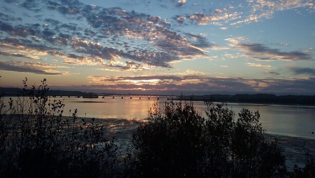 A sunset over a calm body of water with a bridge in the distance. - Bay Bridge Motel (North Bend)