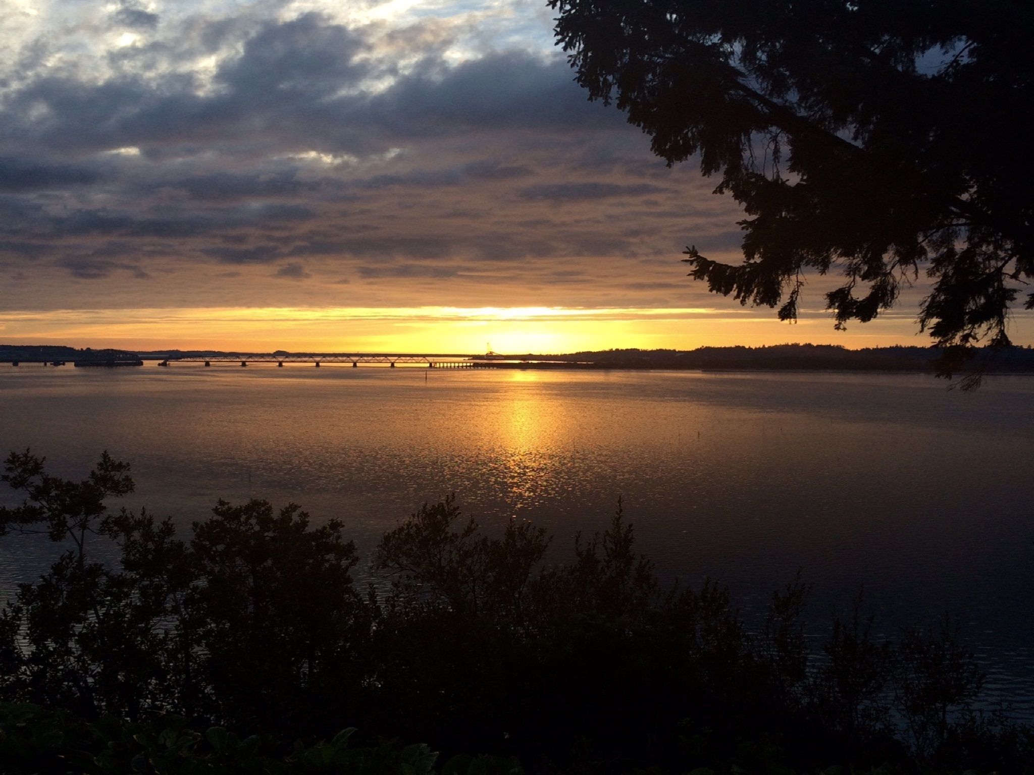 Un atardecer sobre un lago tranquilo con un puente a lo lejos.
