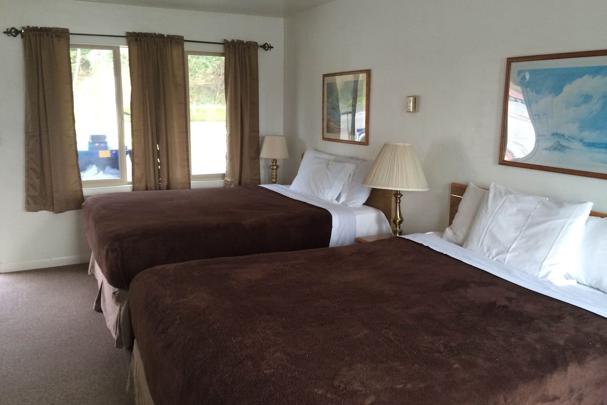 Quarto de hotel com duas camas, uma janela com cortinas, uma luminária, um quadro e um espelho.