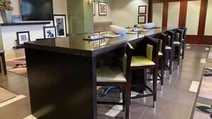 A hotel reception area with a reception desk, bar stools, a flat-screen TV, framed pictures, and a green accent wall. - Hampton Inn by Hilton Leesville Fort Polk (Leesville)