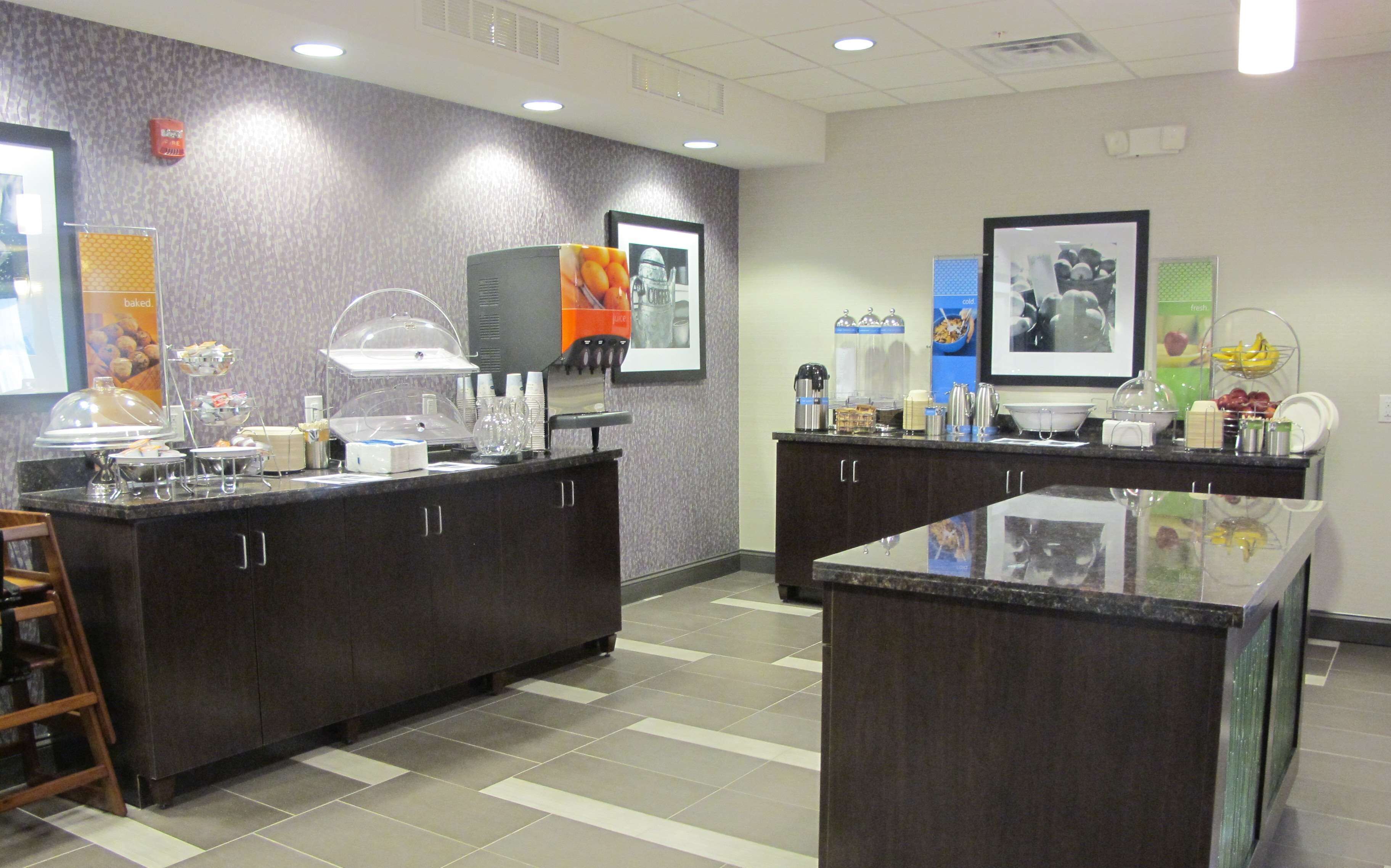 A self-service breakfast area with a variety of food and drink options, including a coffee station and a fruit display.