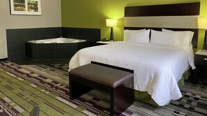 A hotel room with a large bed, a sitting area, a bathtub, and a patterned carpet. - Hampton Inn by Hilton Leesville Fort Polk (Leesville)