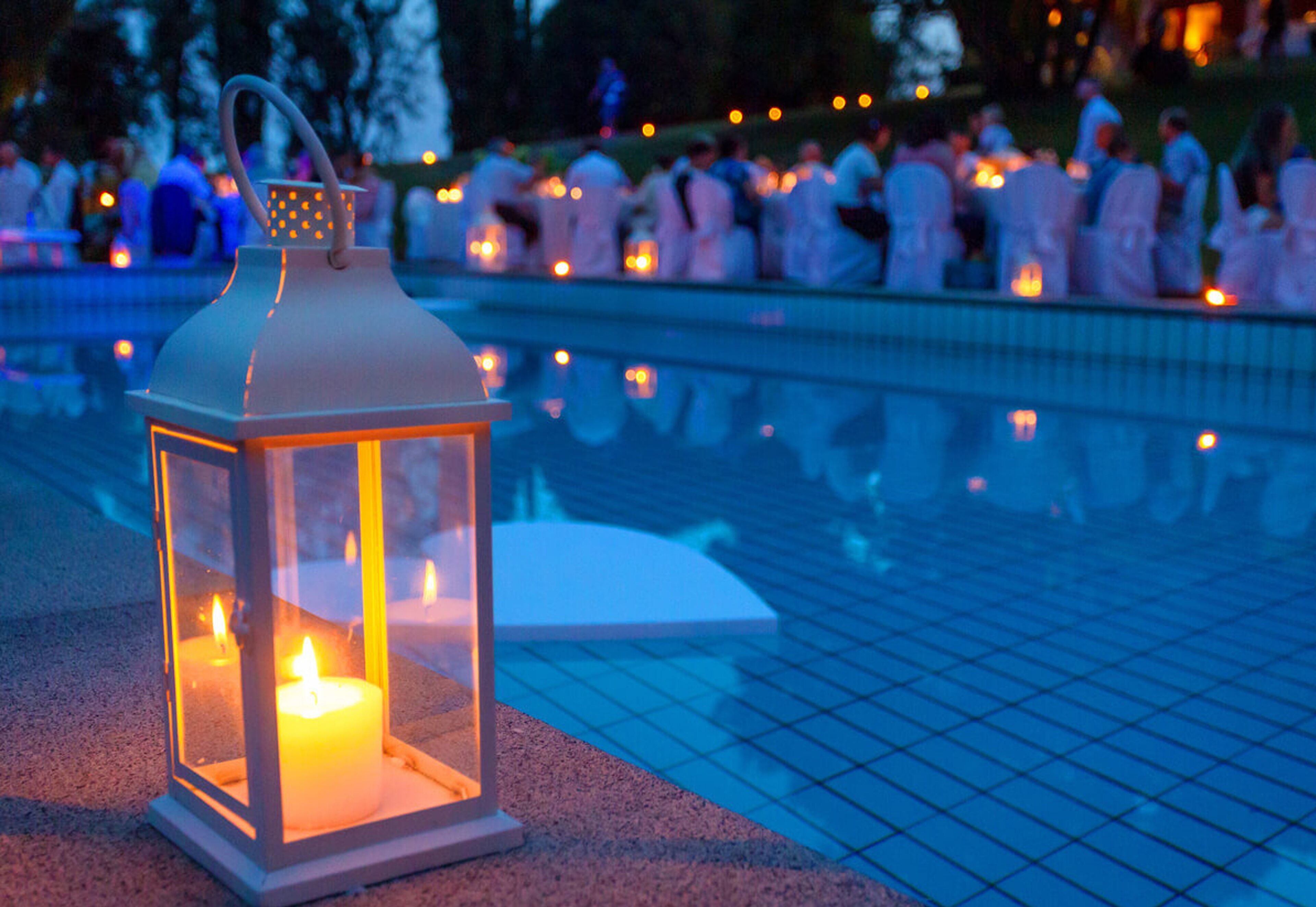 A lantern with a candle inside, placed on a tiled surface near a pool.