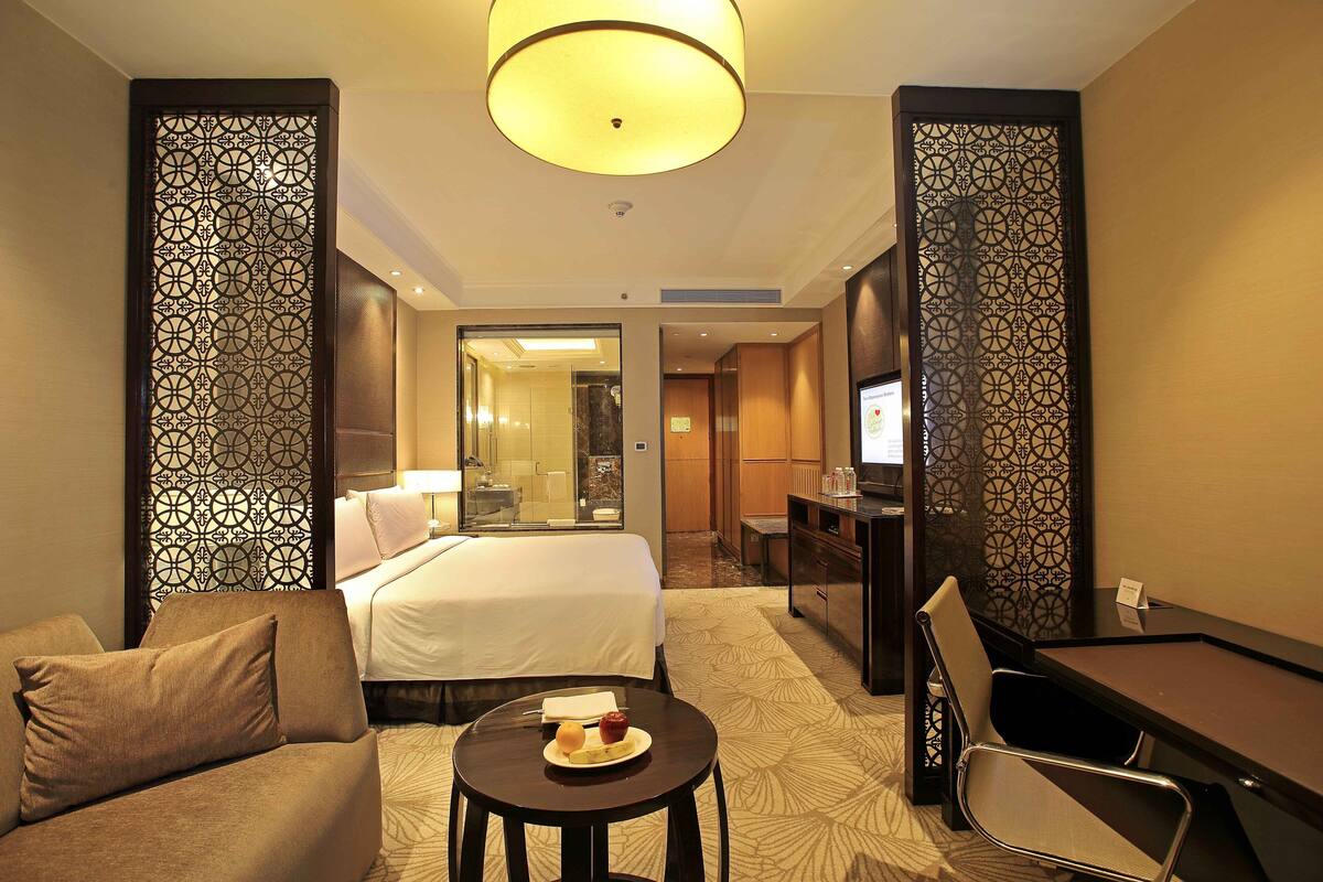 Habitación de hotel con cama, escritorio, sillón, sofá y una mesita con un plato de fruta.