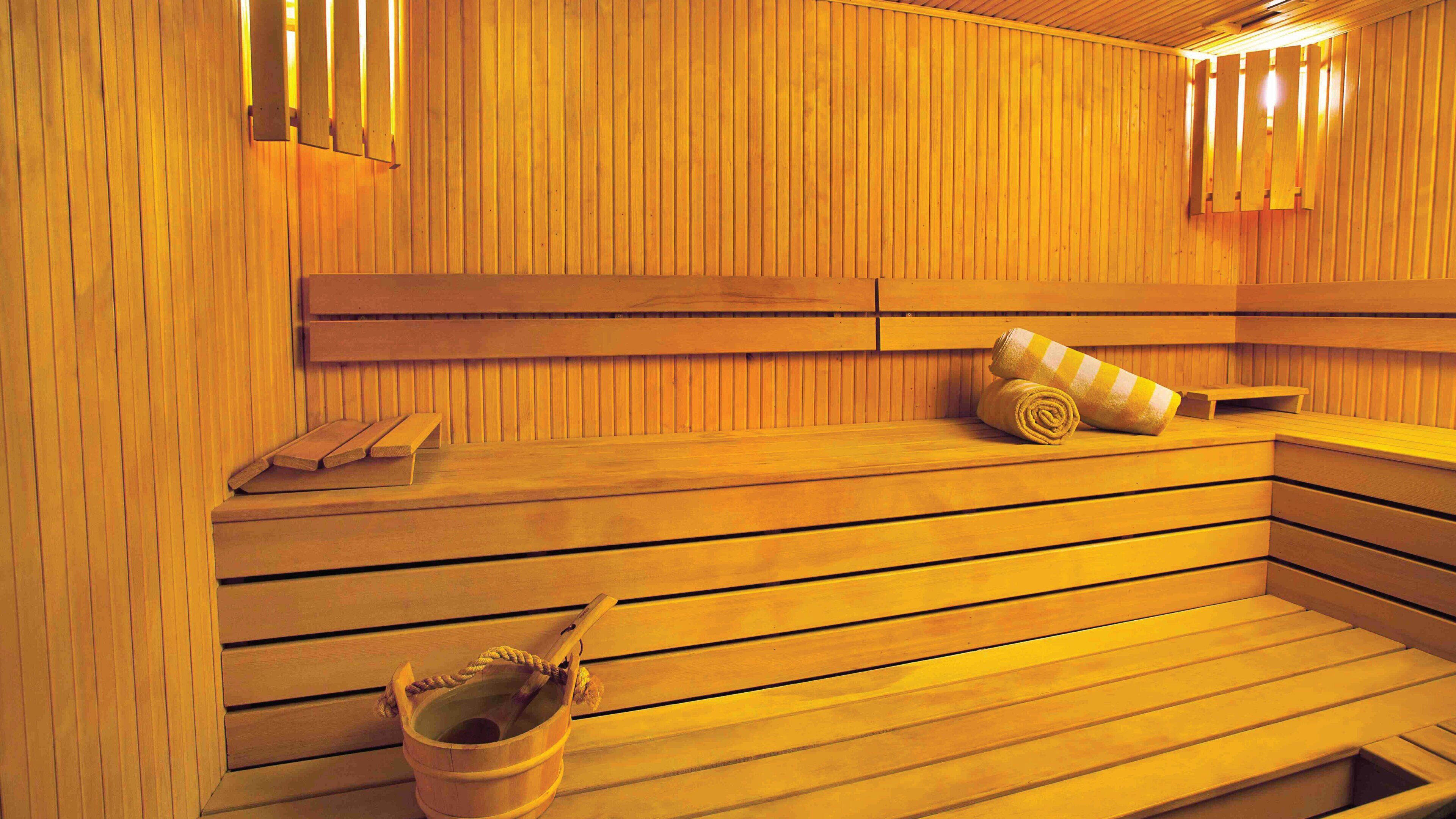 A sauna with wooden benches, a towel, and a bucket.