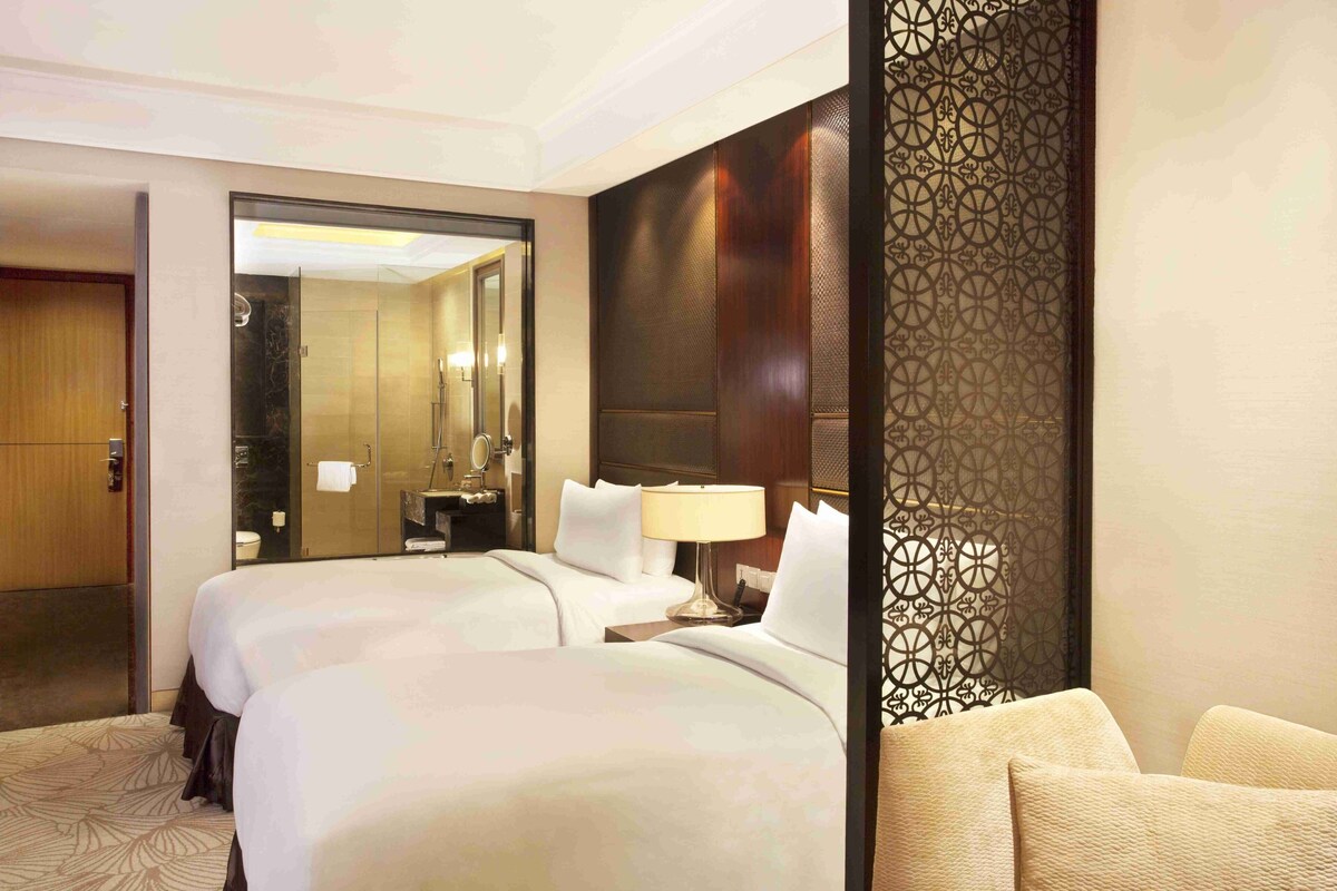 A hotel room with two beds, a bathroom, and a decorative partition.