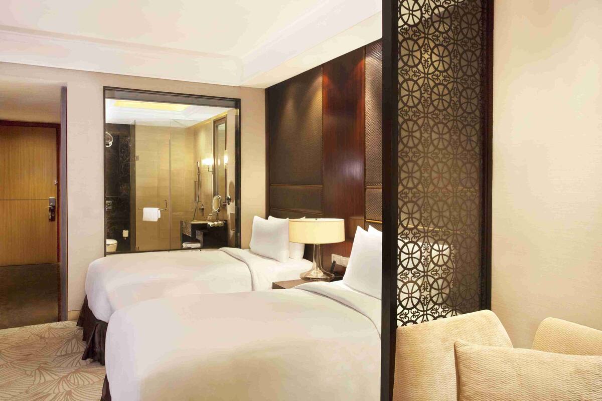 Een hotelkamer met twee bedden, een grote spiegel, een nachtkastje met een lamp en een decoratieve scheidingswand.