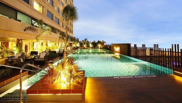A swimming pool with a tiled deck, surrounded by lounge chairs and potted plants. - Crowne Plaza New Delhi Mayur Vihar Noida by IHG (New Delhi)