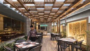 An outdoor dining area with wooden tables and chairs, a bar in the background, and potted plants. - Crowne Plaza New Delhi Mayur Vihar Noida by IHG (New Delhi)