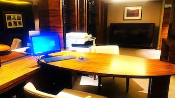 Una habitación de hotel con un escritorio de madera, una computadora, una impresora, un televisor y un sofá.