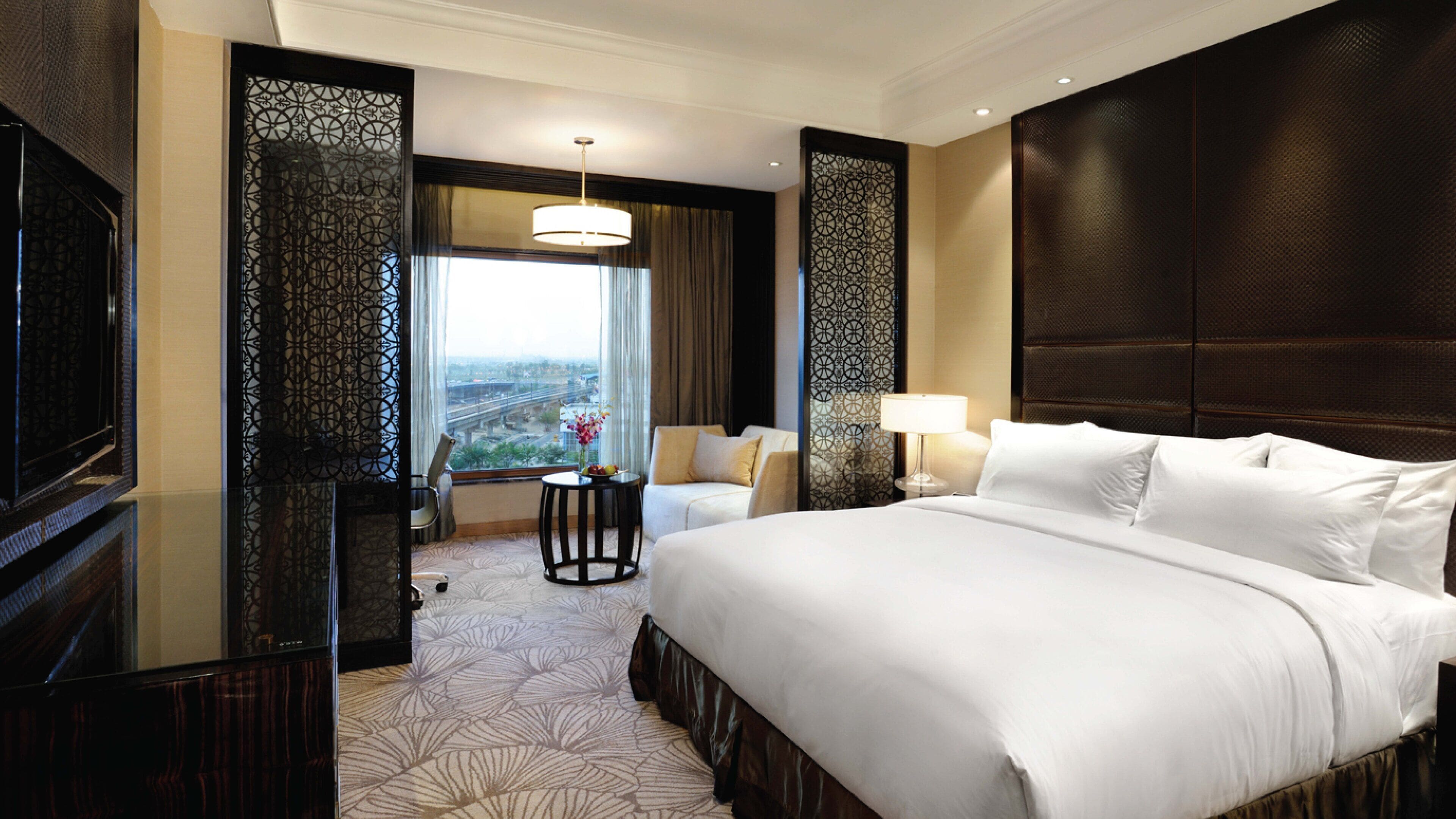 A hotel room with a large bed, a desk, a chair, a window with a view, and a decorative screen.