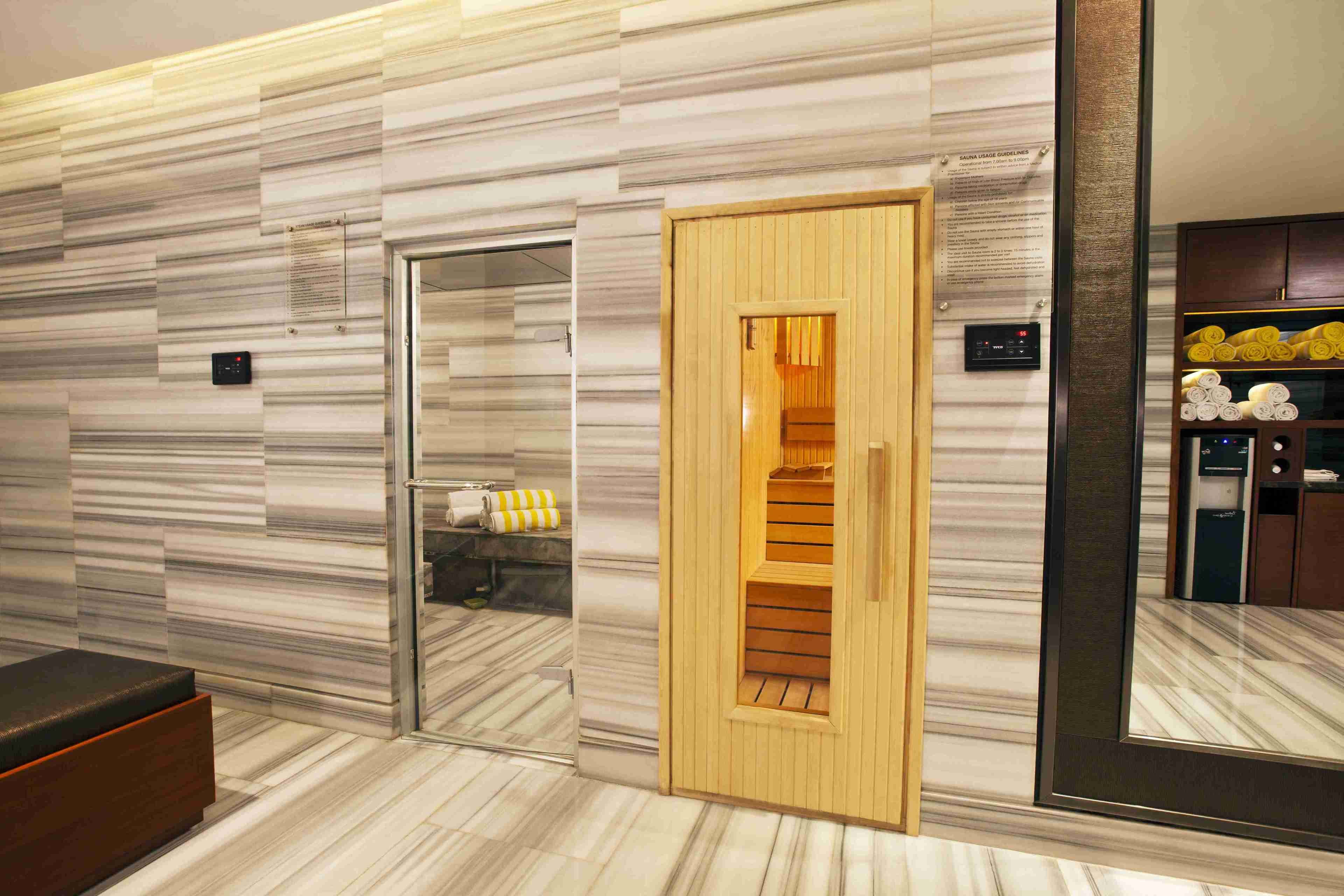 A modern bathroom with a marble wall, a wooden door leading to a shower area, and a bench.