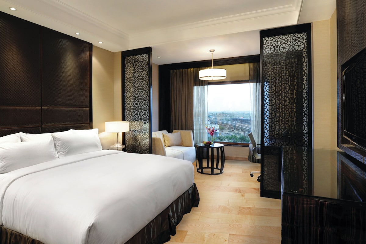 A hotel room with a large bed, a desk, a chair, and a television.