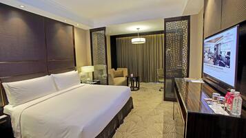 A hotel room with a large bed, a desk with a computer, a chair, a TV screen, and a decorative wall panel.