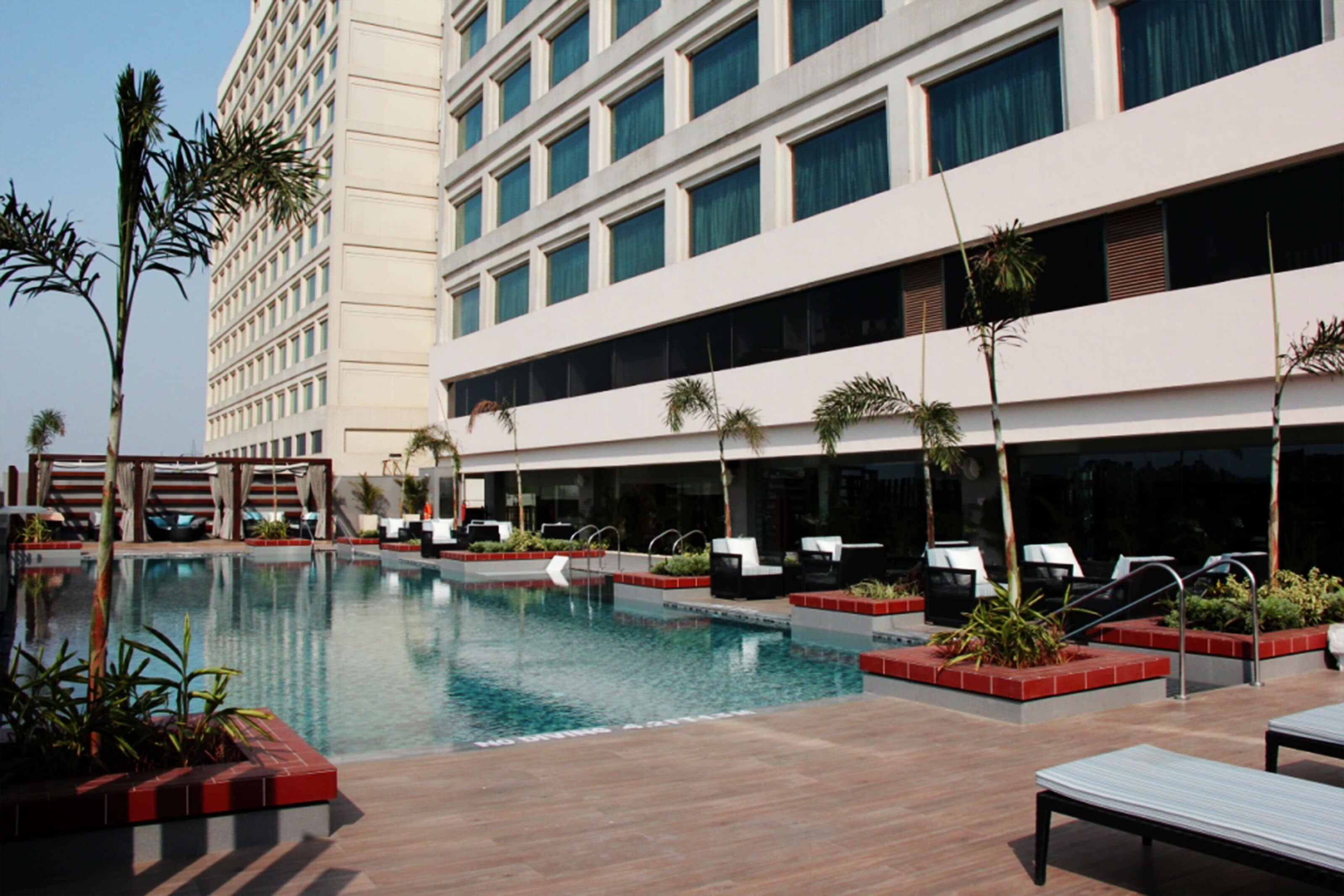 A hotel with a swimming pool, sun loungers, and palm trees.