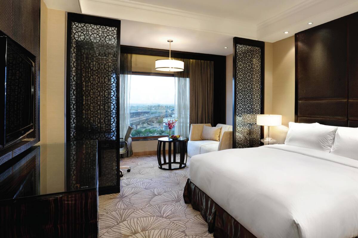 Een hotelkamer met een groot bed, een bureau met stoel, een televisie en een raam met uitzicht op de stad.