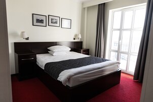 Habitación de hotel con una cama grande, dos mesitas de noche, una ventana con cortinas y tres cuadros en la pared.