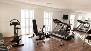A gym with various exercise equipment, large windows, and a wooden floor.