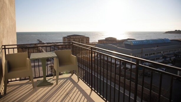 A balcony with a view of the sea, two chairs, and a table.