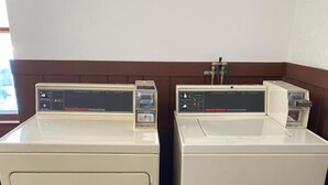 Duas máquinas de lavar roupa frontais brancas numa divisão com pavimento estampado e janela ao fundo.