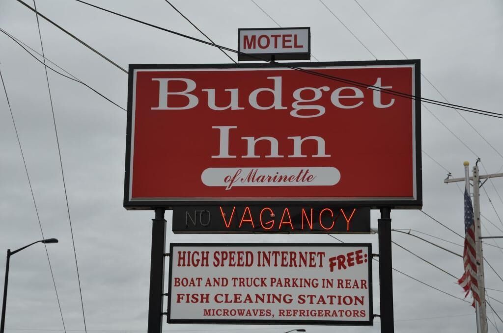 Placa de motel exibindo em destaque 'Budget Inn of Marinette' e 'SEM VAGAS'.