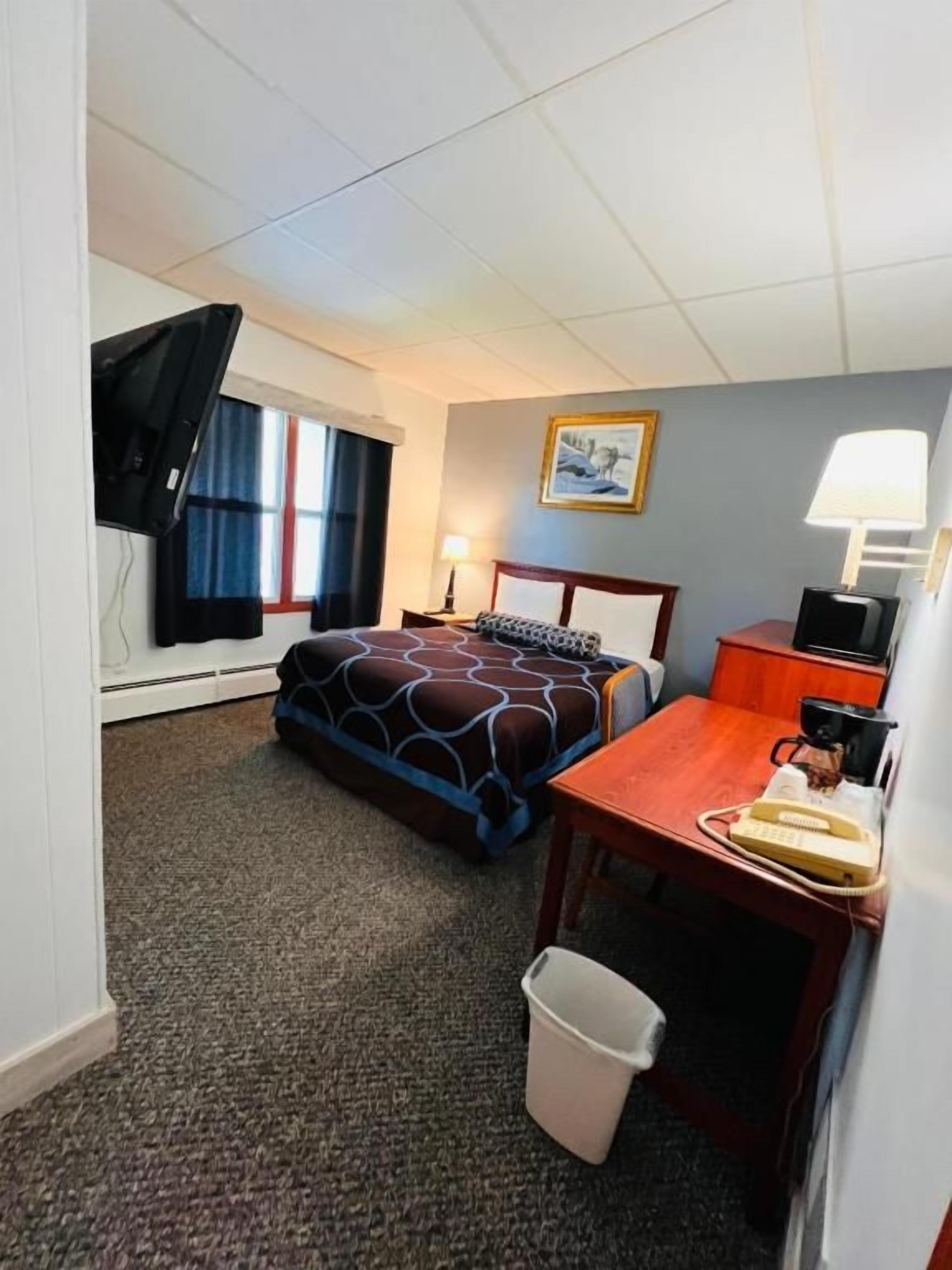 A hotel room with a bed, a desk, a chair, a lamp, a picture on the wall, and a window with curtains.