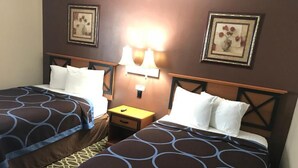 Quarto de hotel com duas camas, cada uma com colcha estampada, mesa de cabeceira com abajur e quadros decorativos nas paredes.
