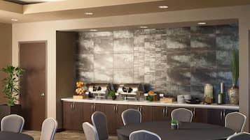A modern conference room with a round table, grey chairs, a kitchen area with a stone backsplash, and a door.