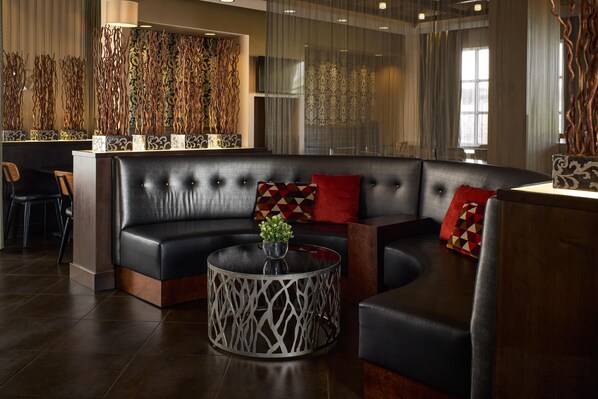 A modern lounge area with a curved black leather sofa, a round glass coffee table, and decorative wall art.