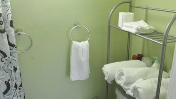 Ett litet badrum med en toalett, en duschdraperi, en handduksställning och en hylla med handdukar och hygienartiklar.