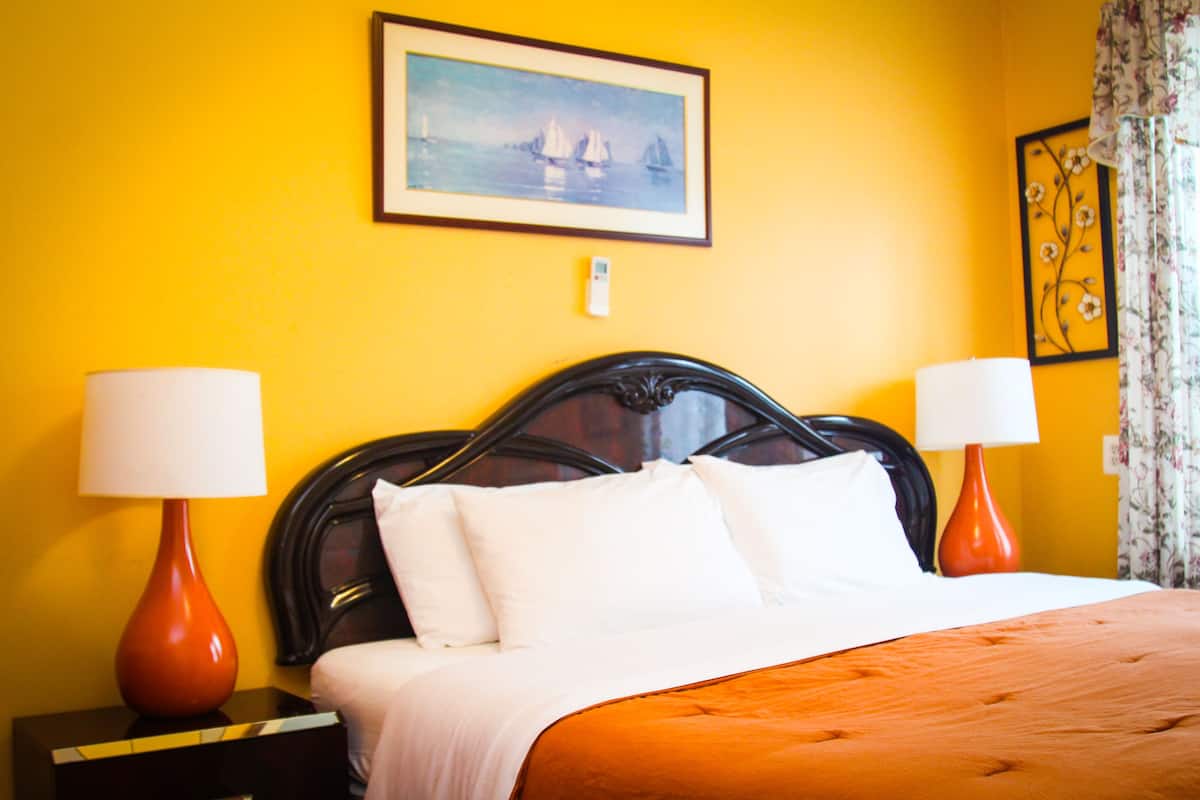 Une chambre d’hôtel avec un lit, deux lampes de chevet, un tableau encadré au mur et un rideau à motifs floraux.