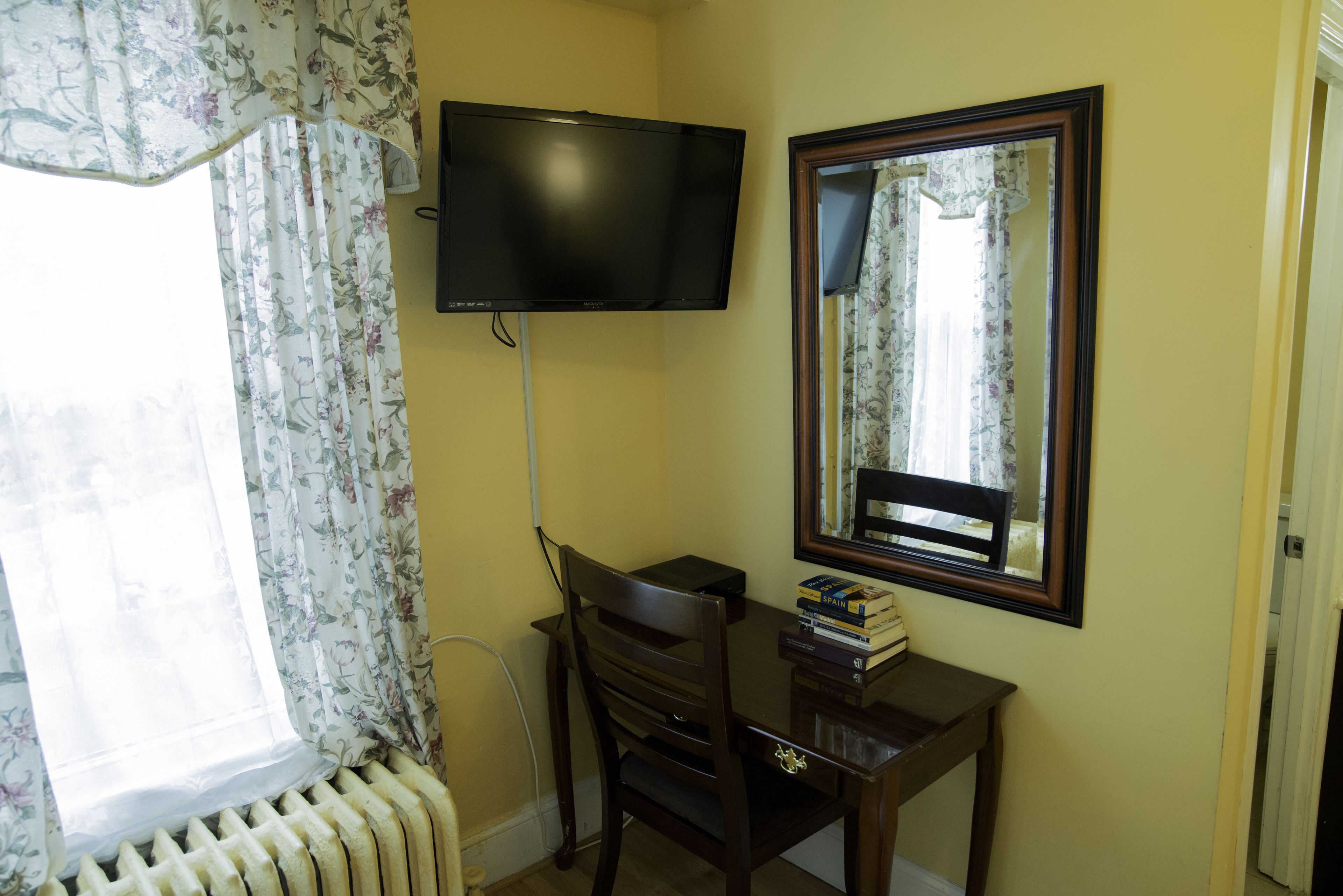 A room with a desk, a chair, a television mounted on the wall, a mirror, and a radiator.