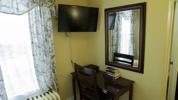 A room with a desk, a chair, a television mounted on the wall, a mirror, and a radiator.