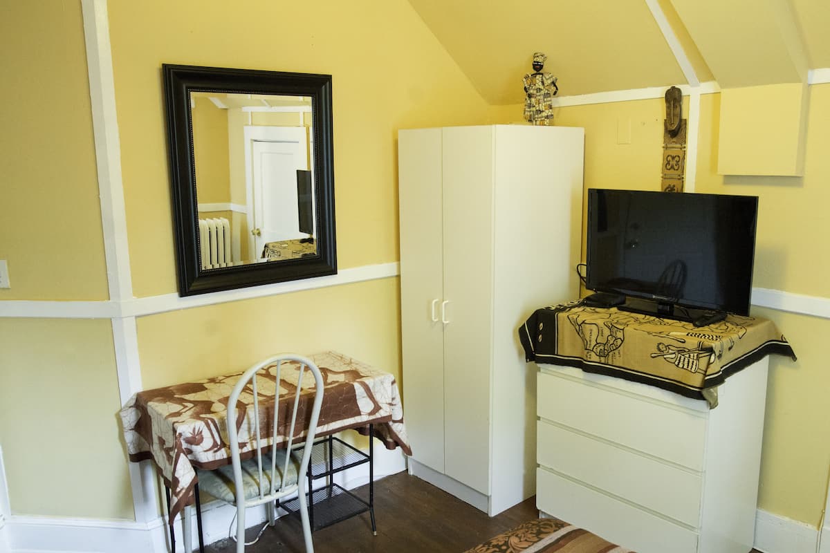 Une pièce comprenant un lit, une table de chevet, une chaise, une armoire, un téléviseur posé sur un meuble et un miroir accroché au mur.
