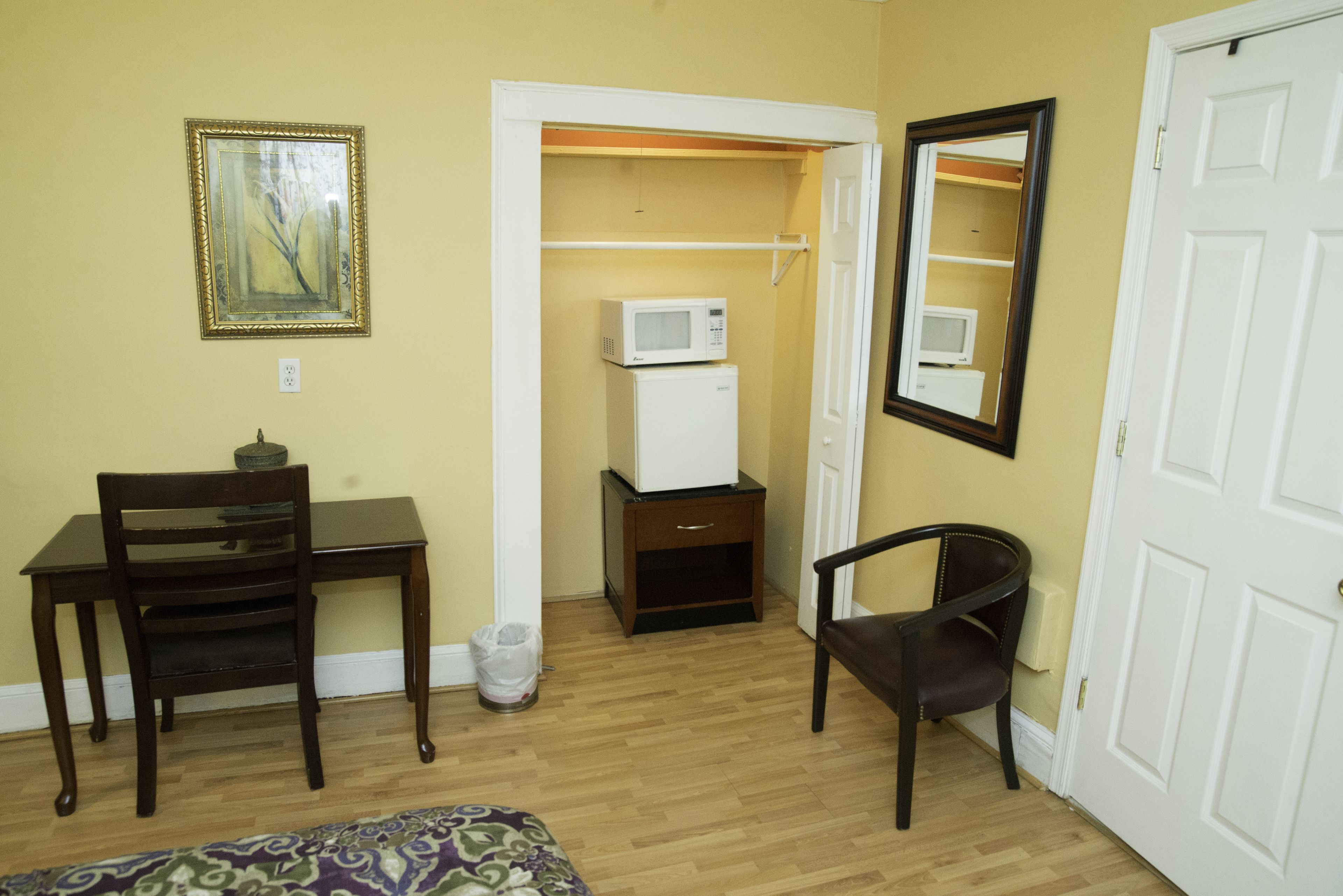 Une pièce comprenant un bureau en bois, une chaise, un lit, un four à micro-ondes, un petit meuble et un miroir.