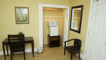 Une pièce comprenant un bureau en bois, une chaise, un lit, un four à micro-ondes, un petit meuble et un miroir.