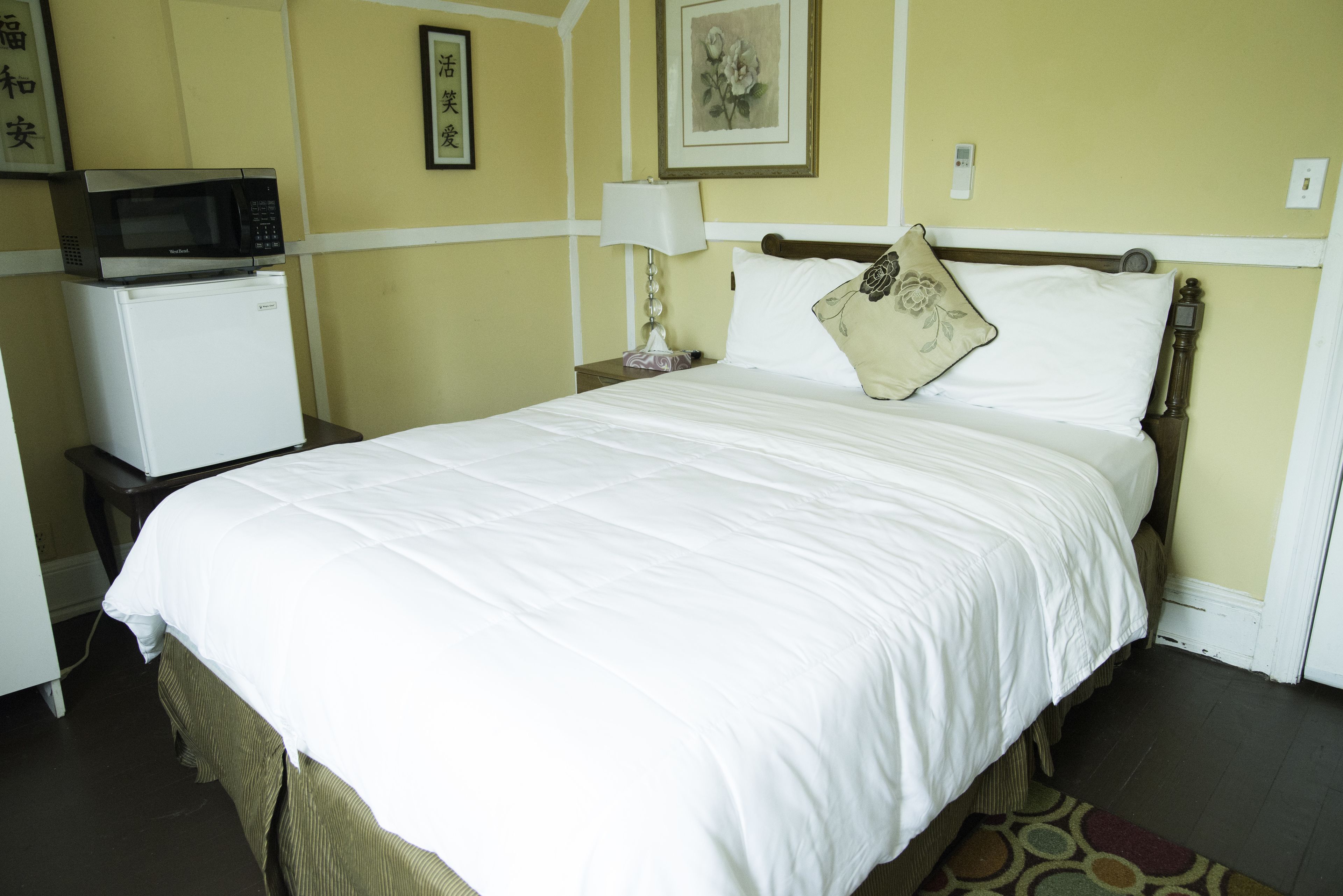 Una habitación de hotel con una cama, una mesita de noche con lámpara, microondas y refrigerador.