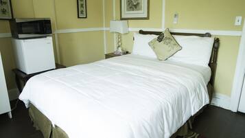 Una habitación de hotel con una cama, una mesita de noche con lámpara, microondas y refrigerador.