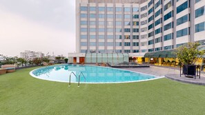A rooftop pool with a grassy area, lounge chairs, and a modern building in the background.