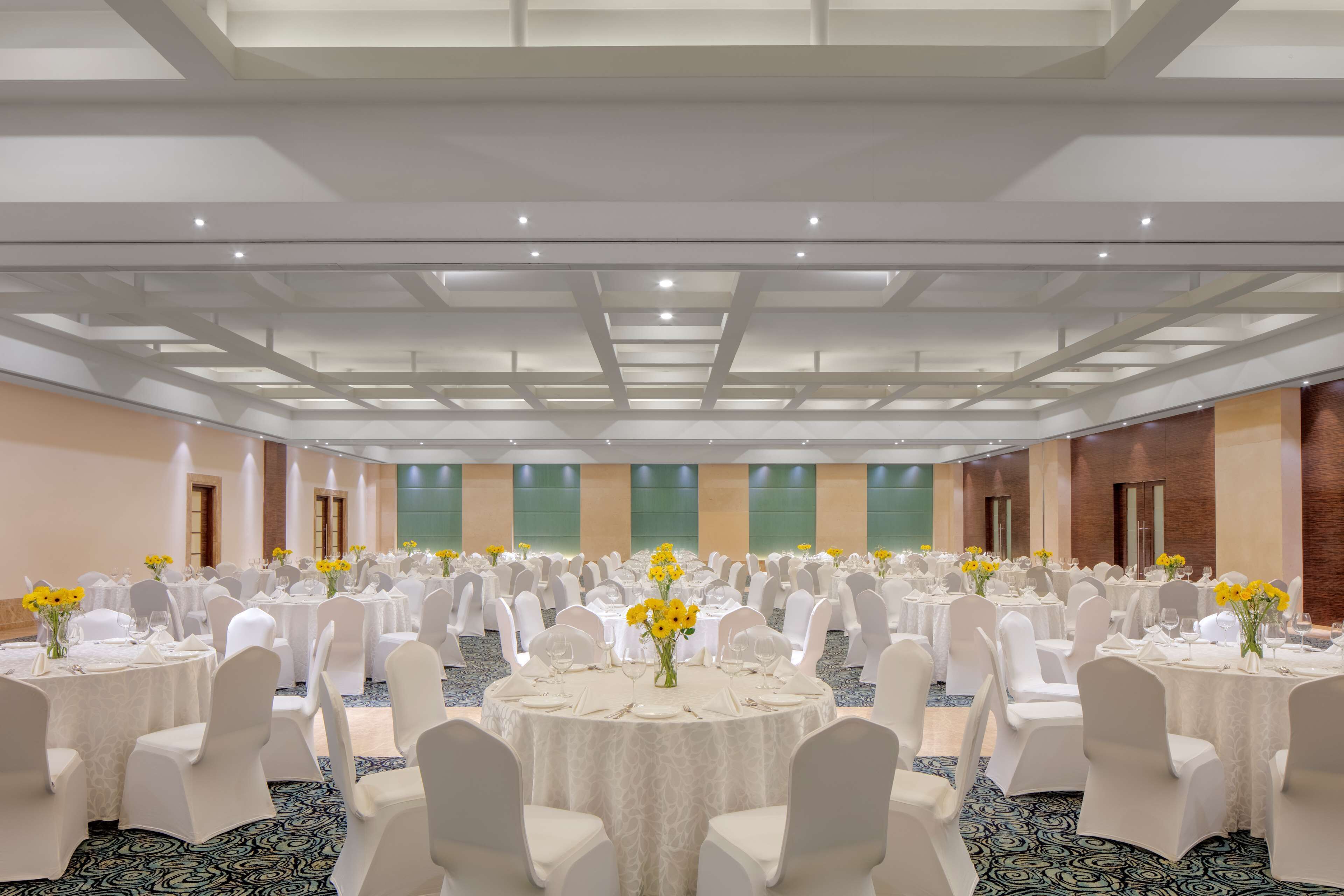Un amplio salón de banquetes con mesas redondas, sillas blancas y flores amarillas.