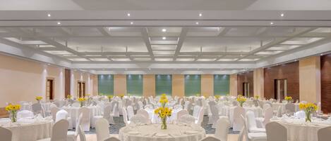 Un amplio salón de banquetes con mesas redondas, sillas blancas y flores amarillas.