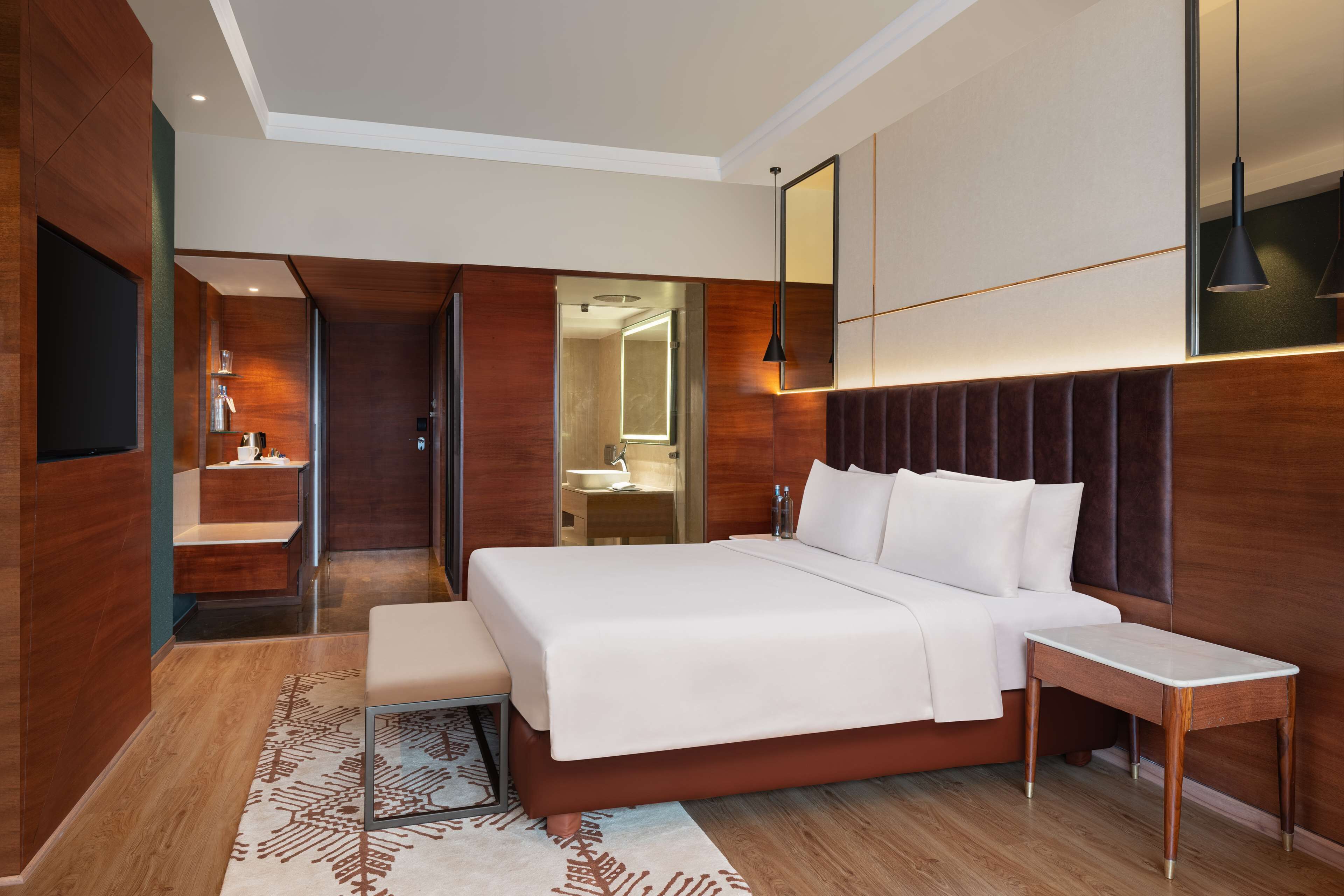 A modern hotel room with a large bed, bedside table, and a mirror above the bed.