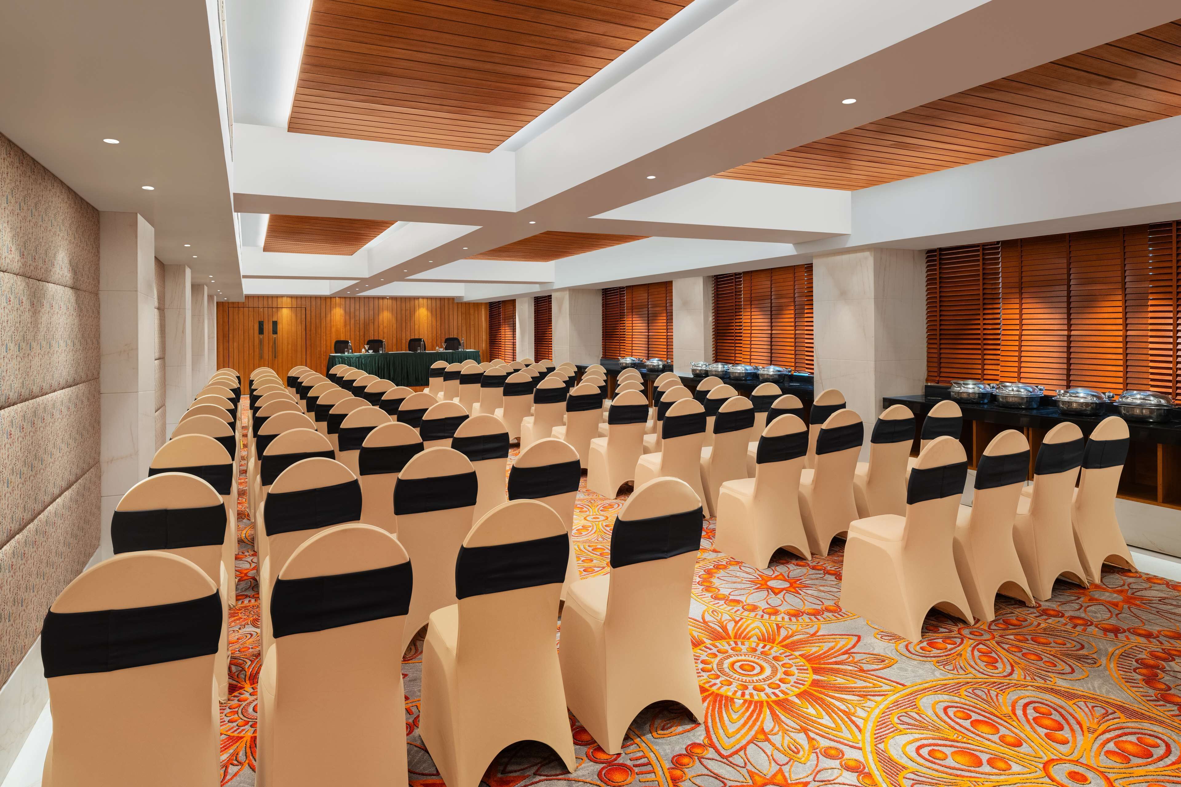 A conference room with rows of beige chairs with black sashes, a long table with a green tablecloth, and a patterned carpet.